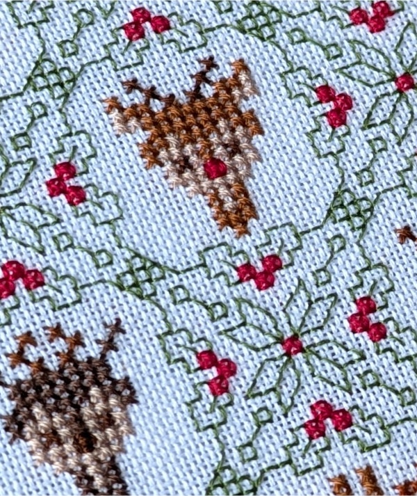 Close up of a stitched cross stitch pattern of all 9 of Santa's reindeer heads with Holly blackwork embroidery elements.