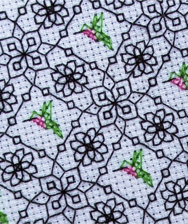 Close up of a stitched blackwork pattern of repeating hummingbirds