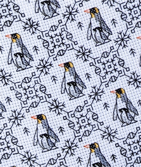 Close up of a stitched cross stitch pattern of mother and baby penguins with Christmas blackwork embroidery elements.